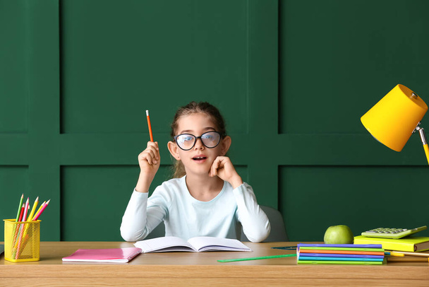 Маленькая девочка делает домашнее задание за столом на цветном фоне - Фото, изображение