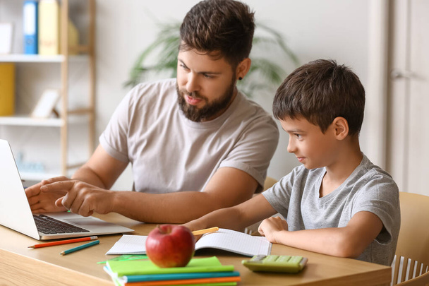 Маленький мальчик со своим отцом делает уроки онлайн дома - Фото, изображение