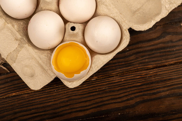 Ovos de galinha branca e um ovo quebrado em uma bandeja feita de papelão branco, foco seletivo de close-up - Foto, Imagem