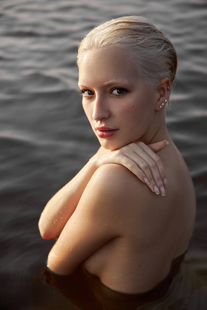Nude naked sexy woman in water at sunset. Beautiful blonde woman with short wet hair and big breasts, art portrait in sea - Photo, image