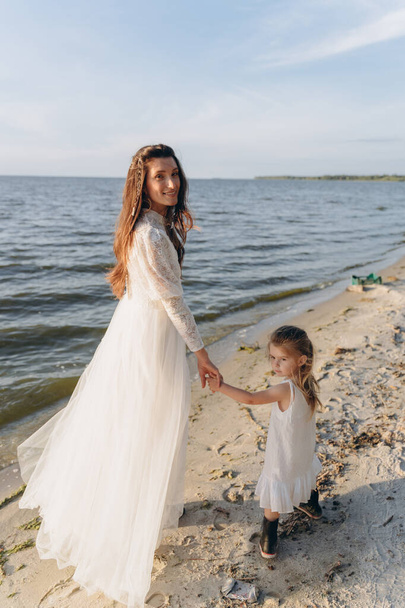 The beautiful photo of mother and little daughter spending time together on river shore near woods - Fotografie, Obrázek