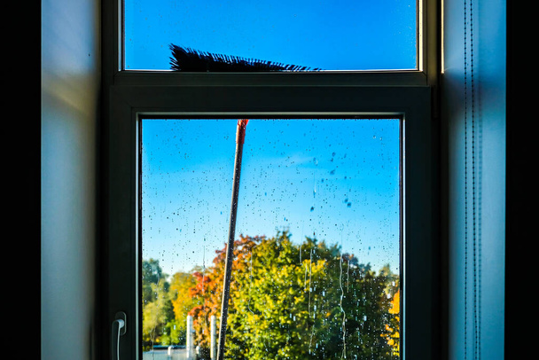 Window cleaning using telescopic water brush and wash system. Commercial window cleaning from the outside with sky in background. Defocused - Photo, Image