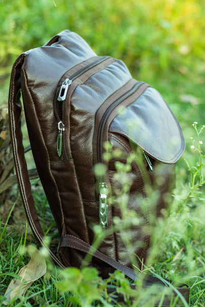 Dark coffee colored leather multifunctional travel bag in the wild green grass - Photo, Image