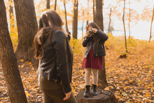 Child girl photographer takes pictures of a mother in the park in autumn. Hobbies, photo art and leisure concept. - Foto, Imagem