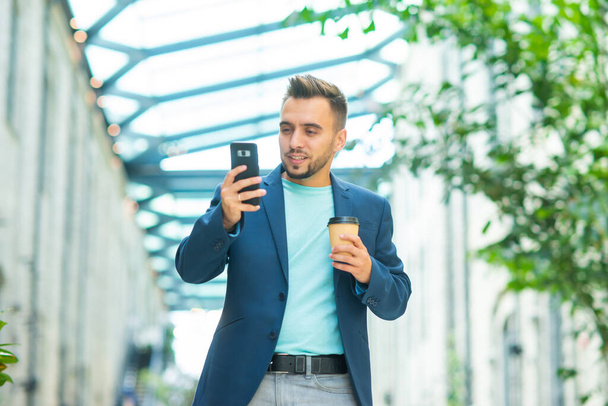 A young successful businessman is working outdoor using smartphone. Man in a casual wear. Business, freelance and remote work. - Photo, Image