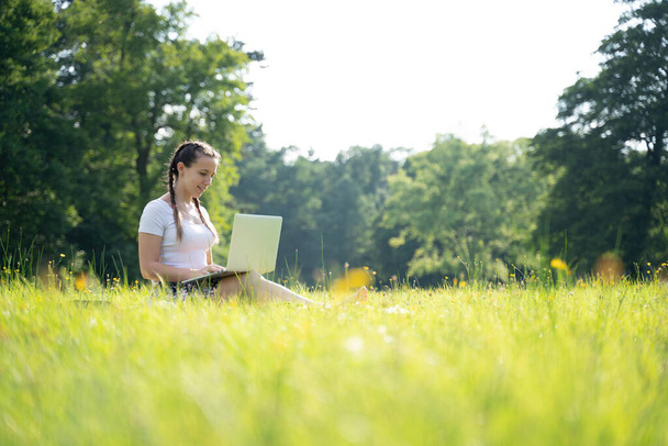 Εξωτερική online επιχειρηματική τεχνολογία. Μαθήτρια εργάζεται κορίτσι με tablet laptop, υπολογιστή στη φύση έξω. Γυναίκα που κάθεται στο καλοκαιρινό πάρκο με ανθρώπους. Happy hipster νέα εξ αποστάσεως μάθηση έννοια - Φωτογραφία, εικόνα