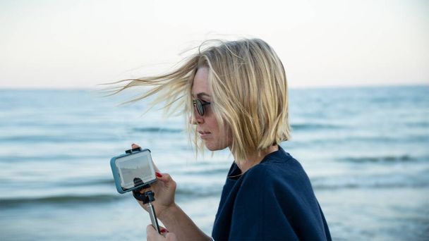Belle fille blogueur prend un blog sur le bord de la mer à l'aide d'un smartphone - Photo, image