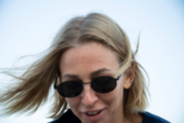 Blurred image of a blonde woman in sunglasses walking on the seashore in a confused mood - Foto, imagen
