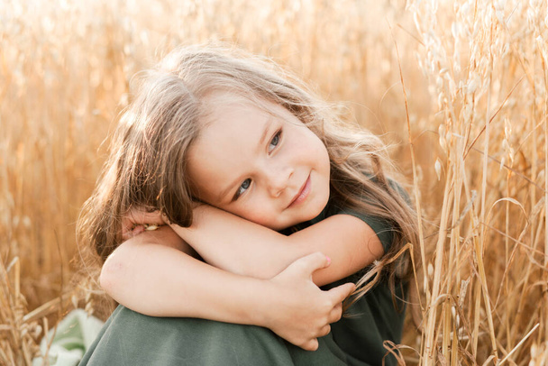Güneşli bir günde buğday tarlasında yürüyen uzun saçlı güzel bir kız. Açık hava portresi. Çocuklar dinleniyor. - Fotoğraf, Görsel