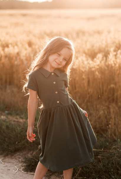 Beautiful little girl with long hair walking through a wheat field on a sunny day. Outdoors portrait. Kids relaxing - Zdjęcie, obraz