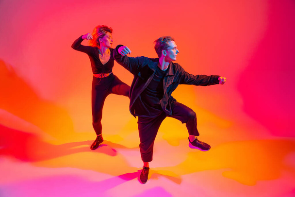 Two beautiful stylish hip-hop dancers, boy and girl on colorful gradient background in neon lights - Фото, изображение