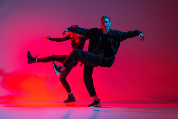Imagen horizontal de pareja joven bailando hip-hop aislada sobre fondo degradado en luz de neón - Foto, imagen