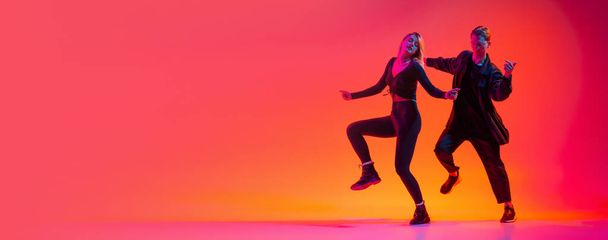 Привлекательный молодой человек и женщина танцующие хип-хоп изолированы на градиентном розовом фоне студии в неоновом свете. Flyer - Фото, изображение