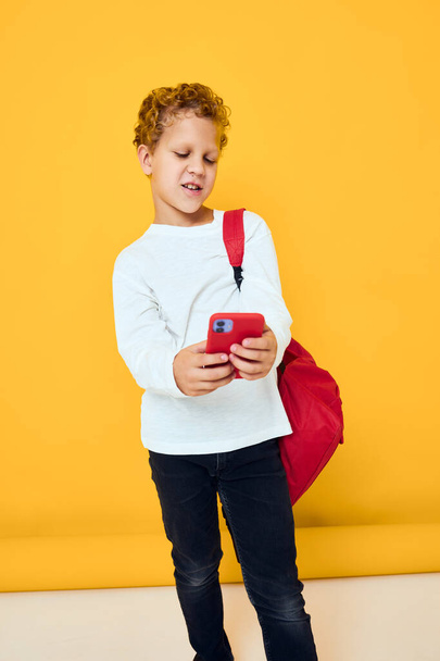 portrait of a little boy in white sweatshirt mobile cell phone red backpack Studio learning concept - Fotó, kép