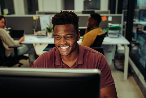 Χαμογελαστός επιχειρηματίας που στέλνει μηνύματα ηλεκτρονικού ταχυδρομείου σε συναδέλφους και διευθυντές που εργάζονται αργά στο γραφείο - Φωτογραφία, εικόνα
