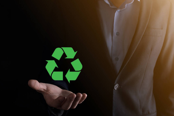 Biznesmen w garniturze na ciemnym tle trzyma ikonę recyklingu, znak w rękach. Ekologia, środowisko i koncepcja ochrony środowiska. Neonowe czerwone niebieskie światło. - Zdjęcie, obraz