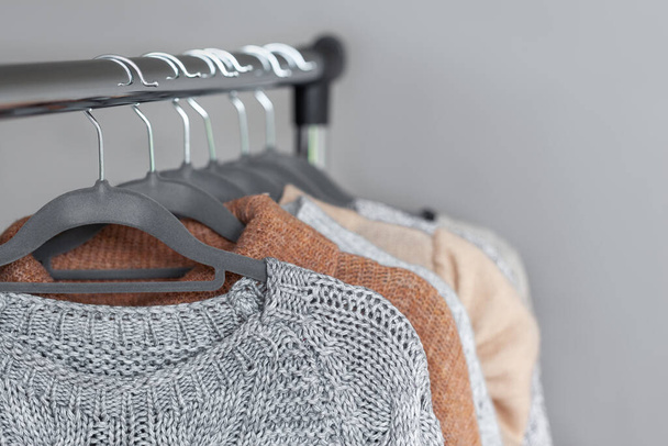 Pastel warm knitted clothes sweater hanging in the closet. Sweaters on gray hangers. Concept cozy autumn and winter wardrobe. - Foto, Imagem