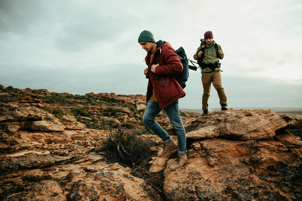 Caucasian male friends hiking in wilderness with backpacks walking together  - Photo, Image