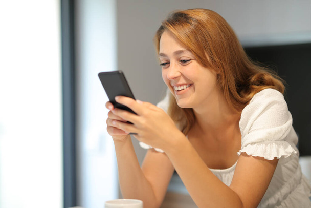 Happy woman using smart phone checking content smiling at home - Фото, изображение