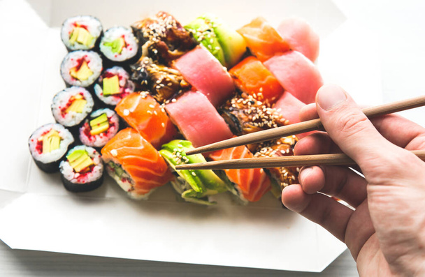 Uomo prende gustoso variopinto assortiti Set di diversi tipi di sushi con bacchette. Cena in stile giapponese. Cibo sano. Rotoli di sushi Filadelfia e Maki con Avocado, Tonno, Salmone, Pesce e Gamberi. - Foto, immagini