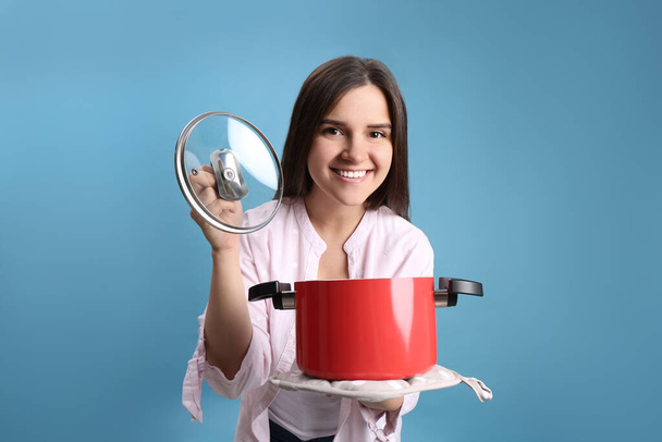 Happy young woman with cooking pot on light blue background - Fotografie, Obrázek