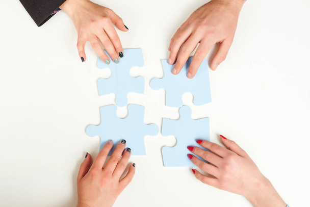 Business people hold in hand a jigsaw puzzle. Business solutions, success and strategy concept. Hands connecting puzzle together on office desk. Group of business people assembling jigsaw puzzle. - Photo, Image