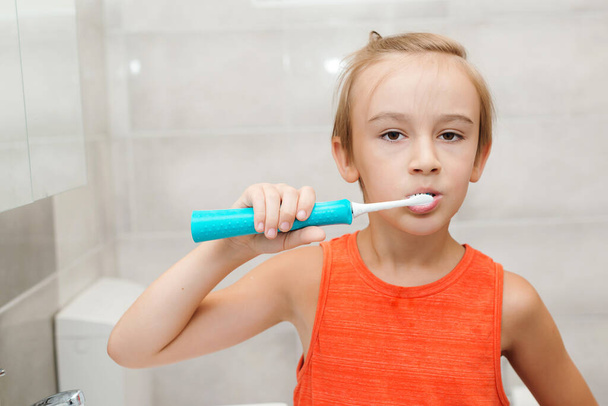 Ребенок чистит зубы электрической щеткой в ванной. Гигиена зубов каждый день. Здравоохранение, детство и гигиена зубов. Мальчик заботится о здоровье своих зубов. Счастливого мальчика чистить зубы. - Фото, изображение