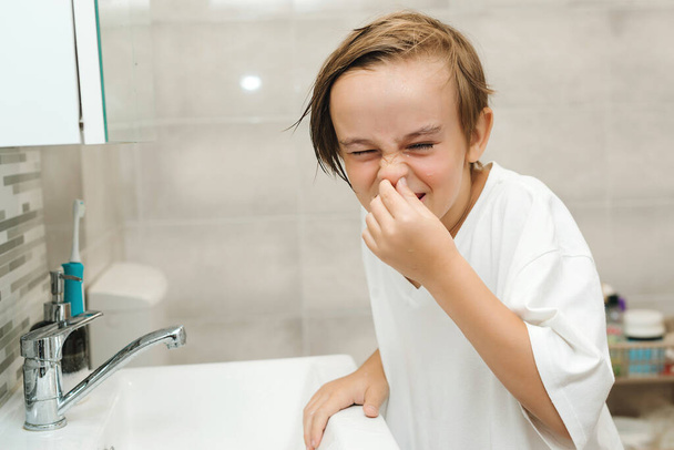 Vicces fiú mossa az arcát a fürdőszobában. Reggeli higiénia. A kaméleon fiút egy mosdókagylóban mossák. Egészséges gyermekkor és életmód. Fogászati higiénia minden nap. Egészségügyi ellátás, gyermek- és fogápolás. - Fotó, kép