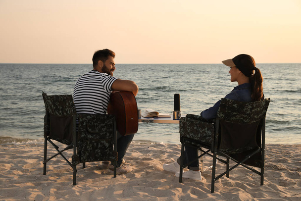 Young man playing guitar to his beloved girlfriend on beach. Camping season - Foto, Bild