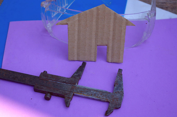 Evaluating home construction costs concept. Building shape with caliper and transparent protection glasses on purple and blue background. - Photo, Image