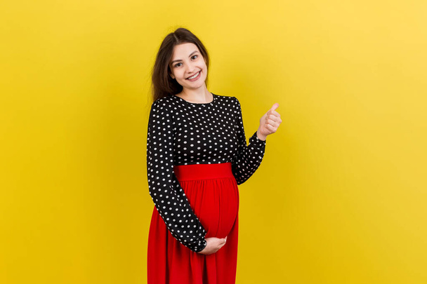 Happy pregnant woman showing thumb up cool gesture over her baby bump at Colored background. Happy maternity. Copy space. - Photo, Image