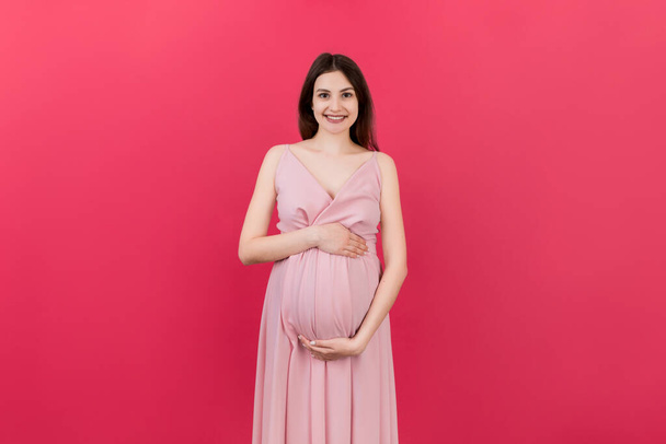 Happy pregnant woman touching her abdomen at Colored background. Future mother. Expecting of a baby. Copy space. - Foto, Imagem