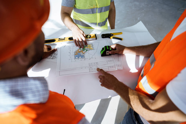 Close up of three man engineers looking at blueprint on construction site - Valokuva, kuva