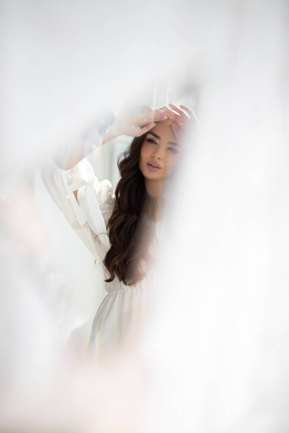 Reflection in the mirror of young pretty brunette girl with incredible makeup in white summer dress. Indoor photography. Blurred photography. - Foto, Imagen