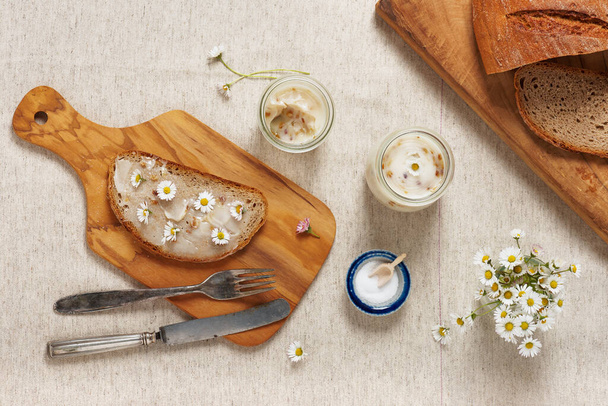 Deliciosa grasa de ganso con pan y flores comestibles de margarita servidas en una tabla de cortar de madera. Vista superior. - Foto, imagen