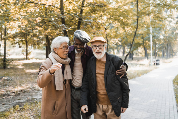 senior afrikaanse amerikaanse man knuffelen interraciale vrienden in bril in de herfst park  - Foto, afbeelding