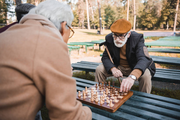 Starsi mężczyźni grający w szachy na ławce w jesiennym parku  - Zdjęcie, obraz