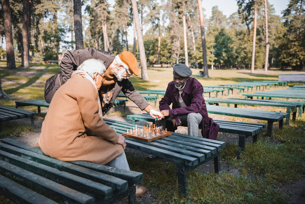 Hommes âgés multiethniques jouant aux échecs sur des bancs dans le parc  - Photo, image