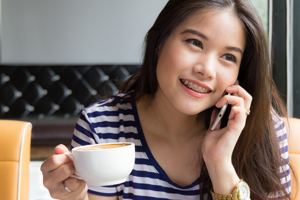 όμορφη γυναίκα, μιλώντας στο τηλέφωνο και κρατώντας το φλιτζάνι του καφέ - Φωτογραφία, εικόνα
