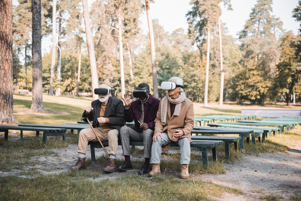 Interraciale oude vrienden met smartphone met behulp van virtual reality headsets in het park  - Foto, afbeelding