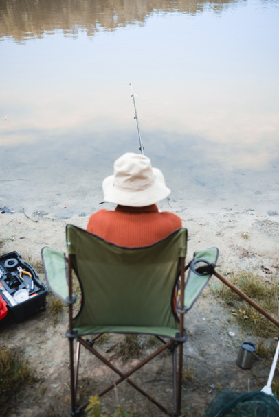 Back view of blurred senior man fishing near walking cane and lake on coast - Foto, immagini