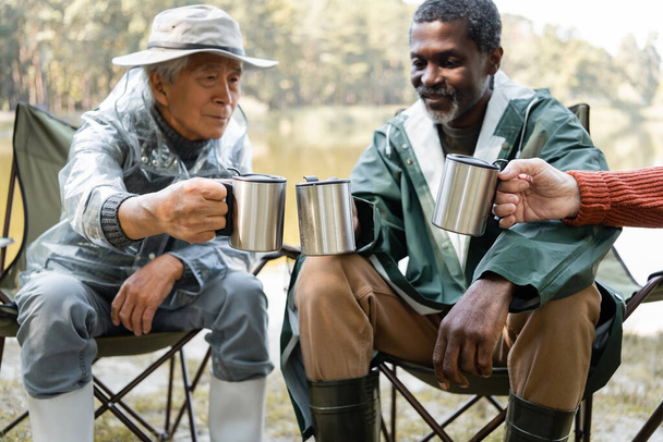 Розмиті старші друзі в рибальському вбранні тримають термо чашки на відкритому повітрі
  - Фото, зображення