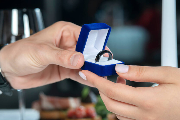 Male hands with blue velvet box containing payments smart ring. Man gives a woman payments smart ring.  Romantic dinner. Valentine day - Foto, afbeelding