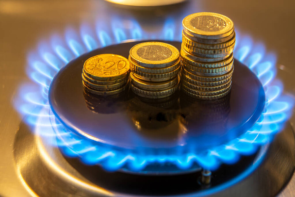 Gas stove lit, with stacks of coins above it. Increase in gas costs and tariffs. - Photo, Image