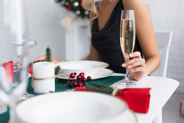 partial view of woman with glass of champagne sitting at festive table - Foto, afbeelding
