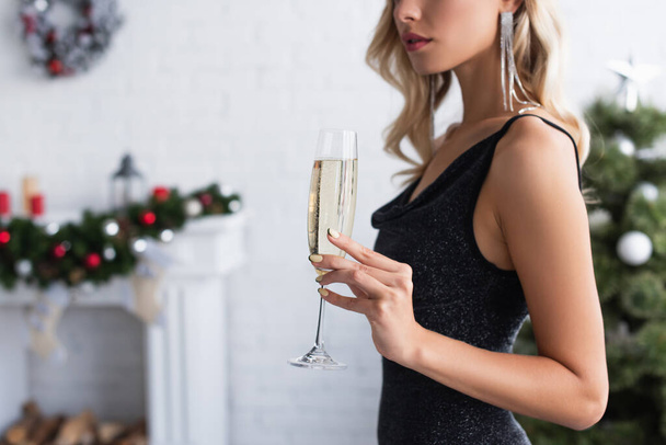 partial view of elegant woman with champagne glass in living room with blurred christmas decoration - Fotoğraf, Görsel