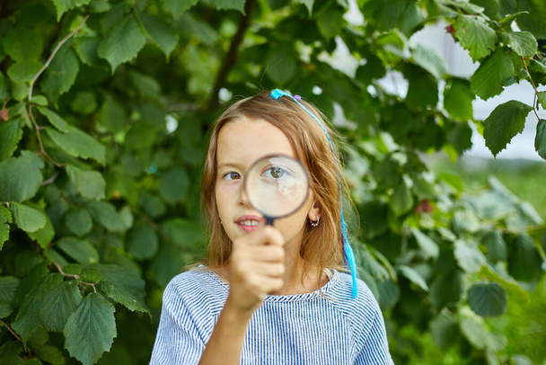 Klein meisje speelt met een vergrootglas in haar achtertuin thuis trek gezichten. Leefstijlconcept voor kinderen, onderwijs, schoolconcept - Foto, afbeelding