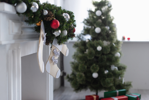 fireplace decorated with spruce garland and christmas stockings near blurred christmas tree - Photo, Image