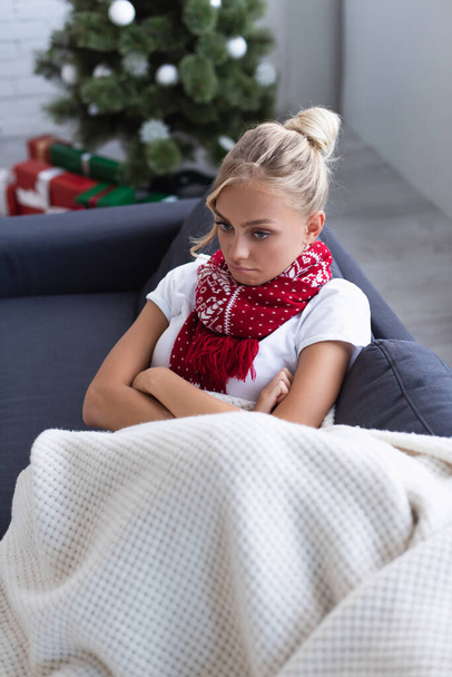 high angle view of sick and upset woman with crossed arms on sofa near christmas tree on blurred background - Foto, Imagem