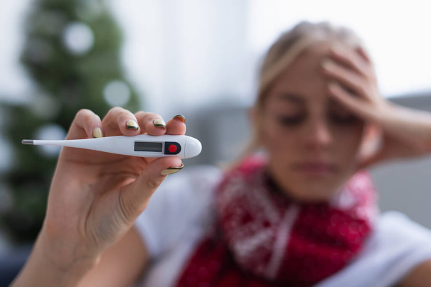 selective focus of electronic thermometer in hand of sick woman on blurred background - Foto, afbeelding